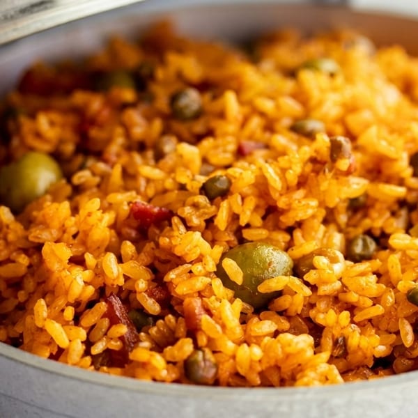 Close-up of vibrant orange rice with green olives and peas in a metal pot.