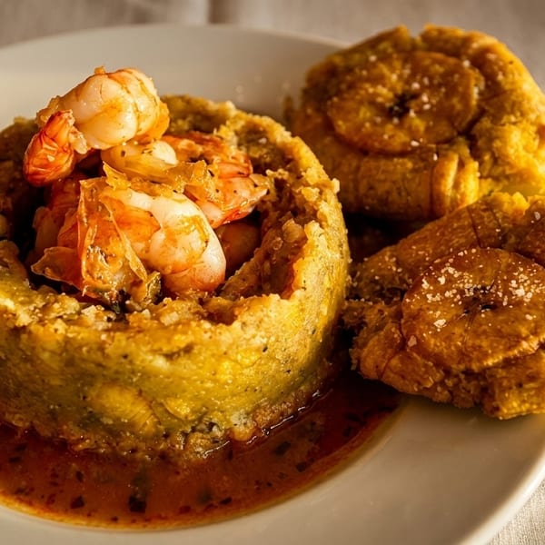 Mofongo with shrimp in a savory sauce, served with crispy tostones on a white plate.